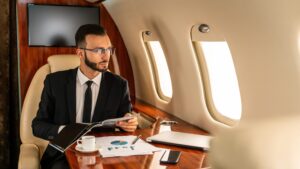 Business man looking out the window of a private jet while reading a magazine.